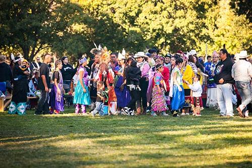 Many people, some in traditional garb, gathering on the Fort Omaha Fairgrounds